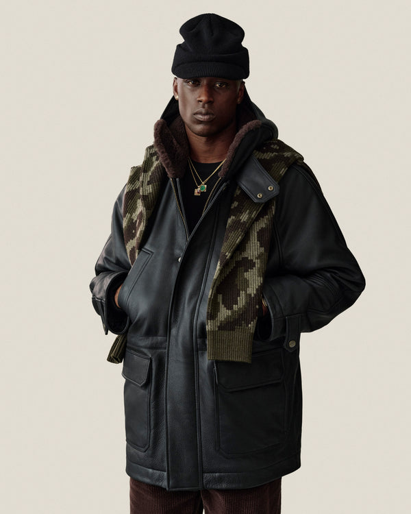 A person wearing a black Wool Brim Beanie, a black shearling-lined leather jacket, and a camouflage print scarf.