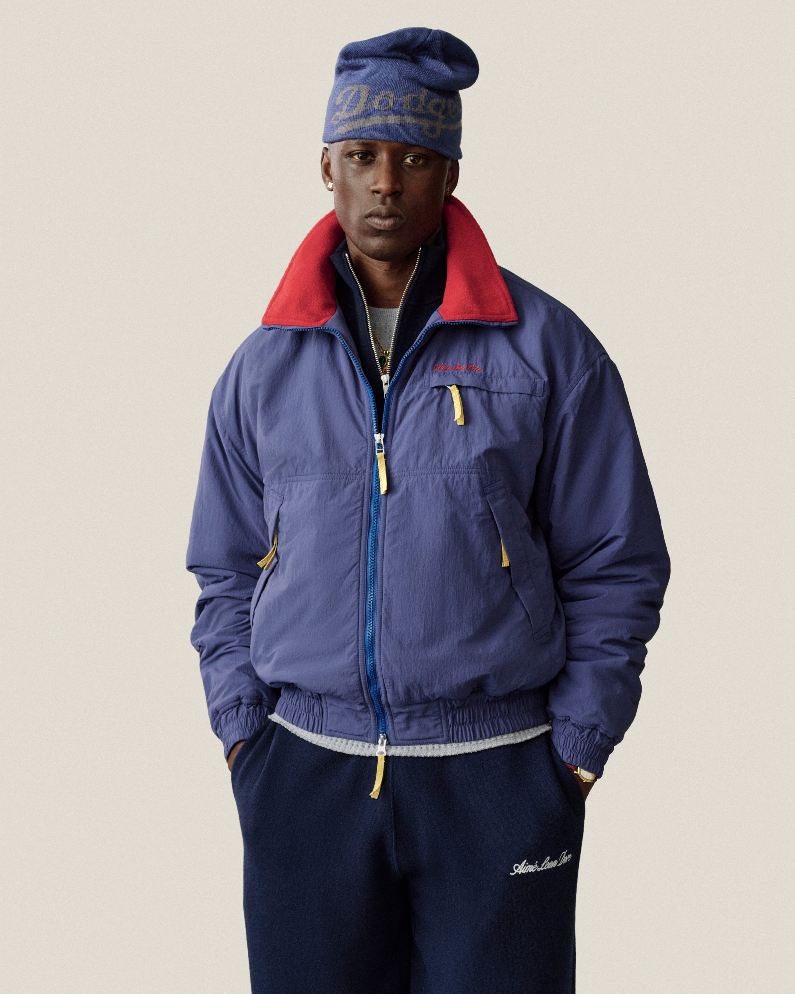 A man wears an ALD / New Era Dodgers Beanie and a blue zip-up jacket with a red collar.