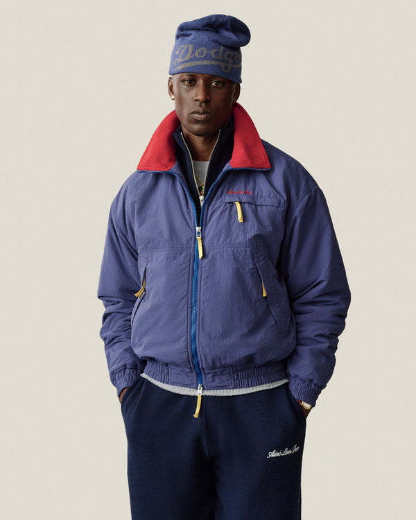 A man wears an ALD / New Era Dodgers Beanie and a blue zip-up jacket with a red collar.