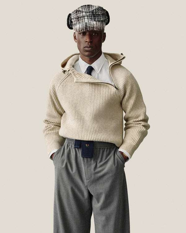 A man in a plaid cap, white shirt, cream hooded sweater, and a navy Crest Silk Knit Tie.