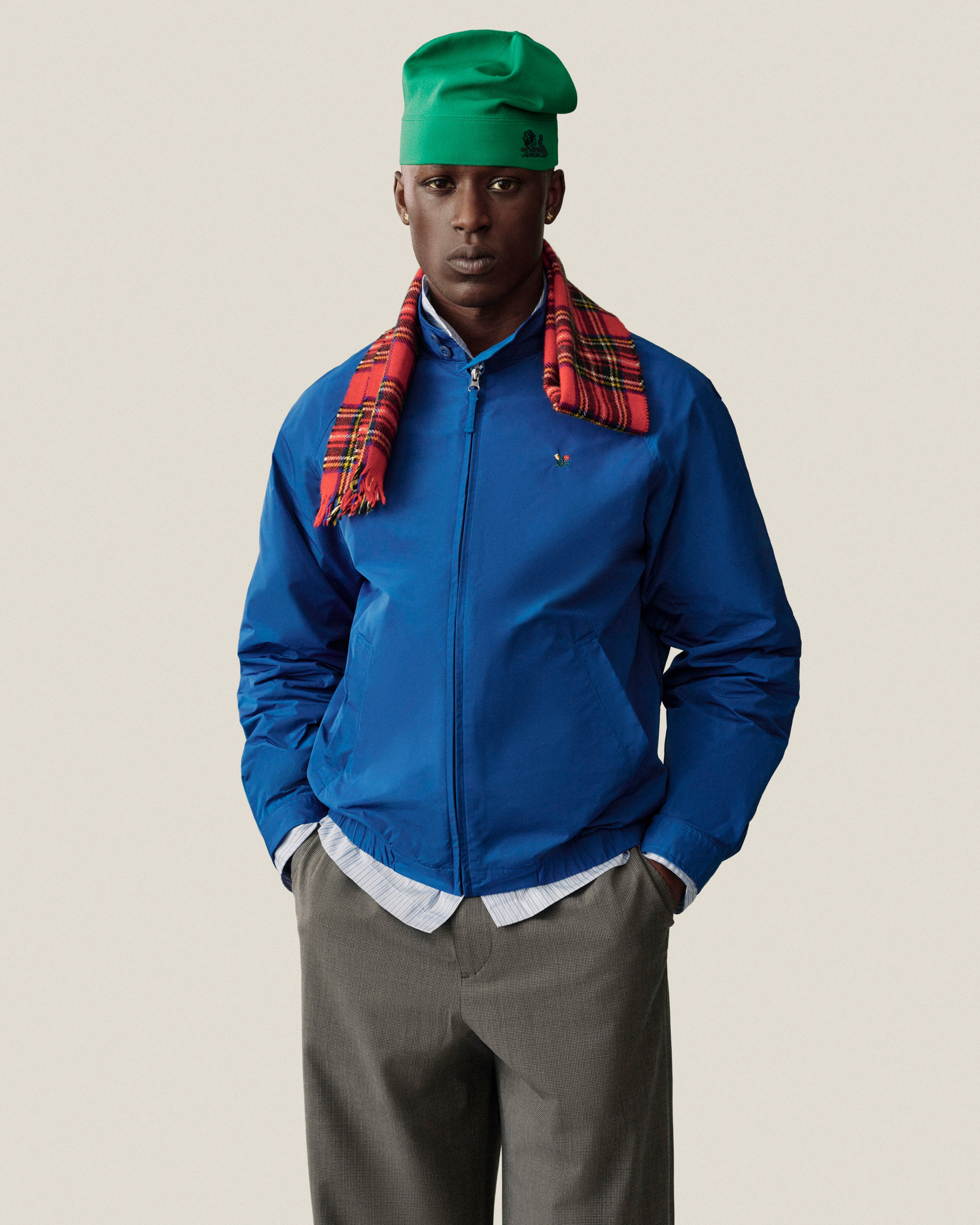 Model in Crest Nylon Windbreaker, gray trousers, green hat, and red plaid scarf poses against a plain background.