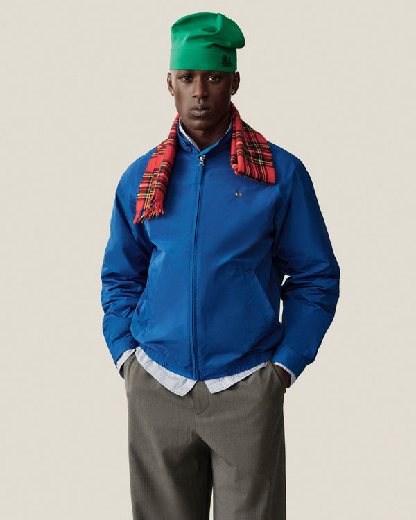 Model in Crest Nylon Windbreaker, gray trousers, green hat, and red plaid scarf poses against a plain background.