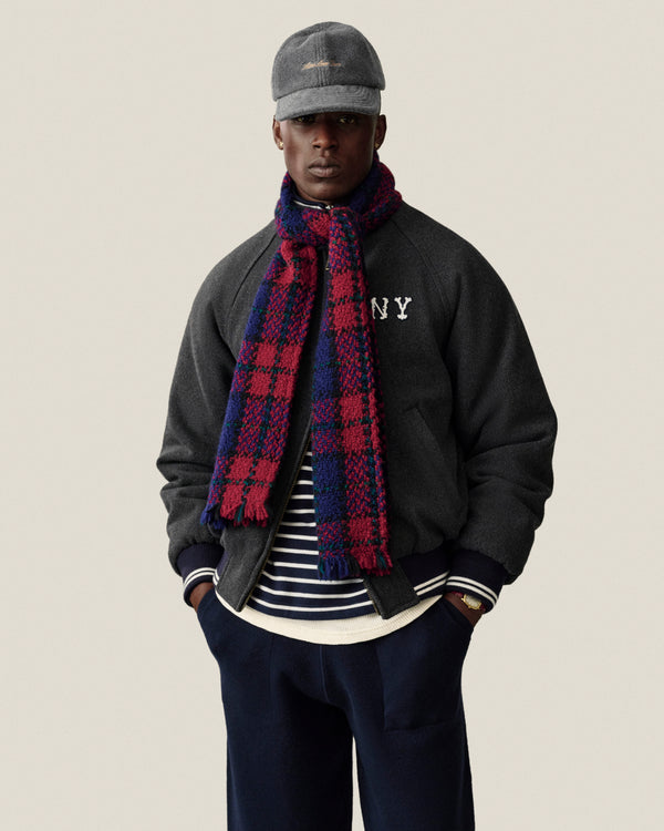 A man in a NY Highlanders Wool Varsity Jacket stands with hands in pockets against a plain background.