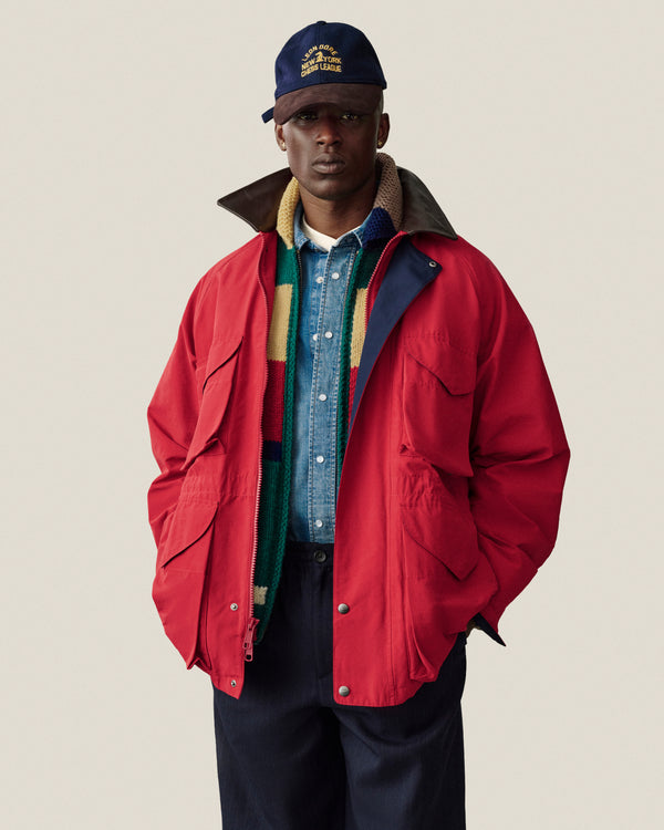 Man in a Lightweight Barn Jacket, blue shirt, scarf, navy pants, and cap stands against a plain background.