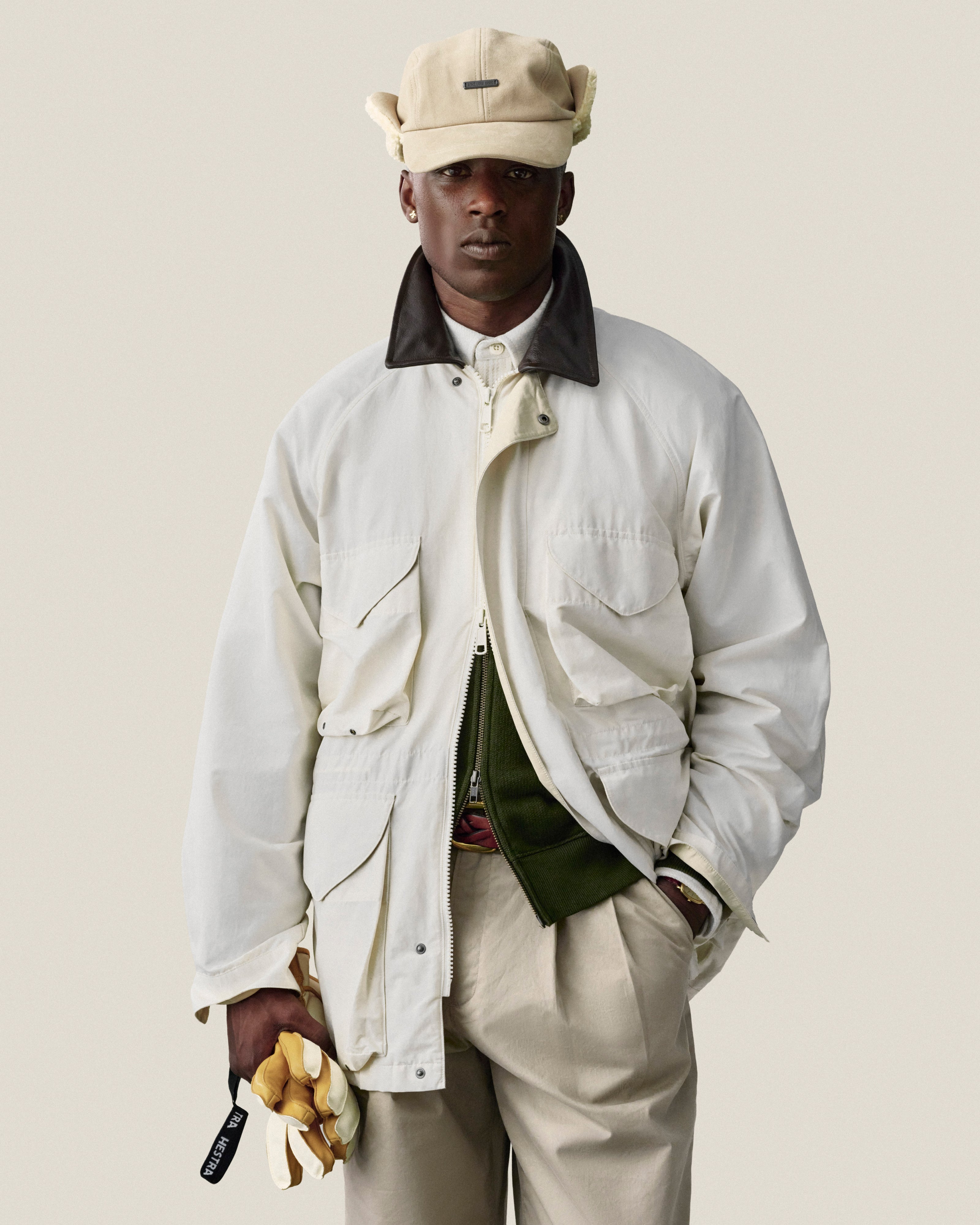 A man in a Lightweight Barn Jacket, beige cap, and tan pants holds yellow gloves against a plain background.