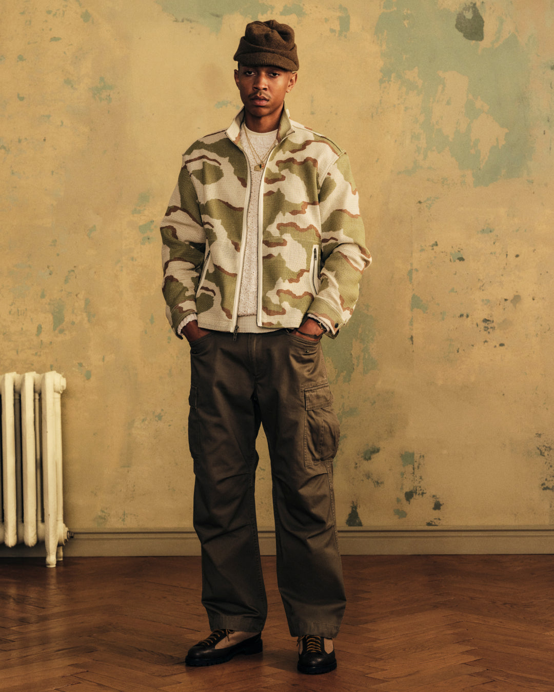 A person wearing a brown Wool Brim Beanie, camouflage zip-up jacket, cream sweater, and olive cargo pants.