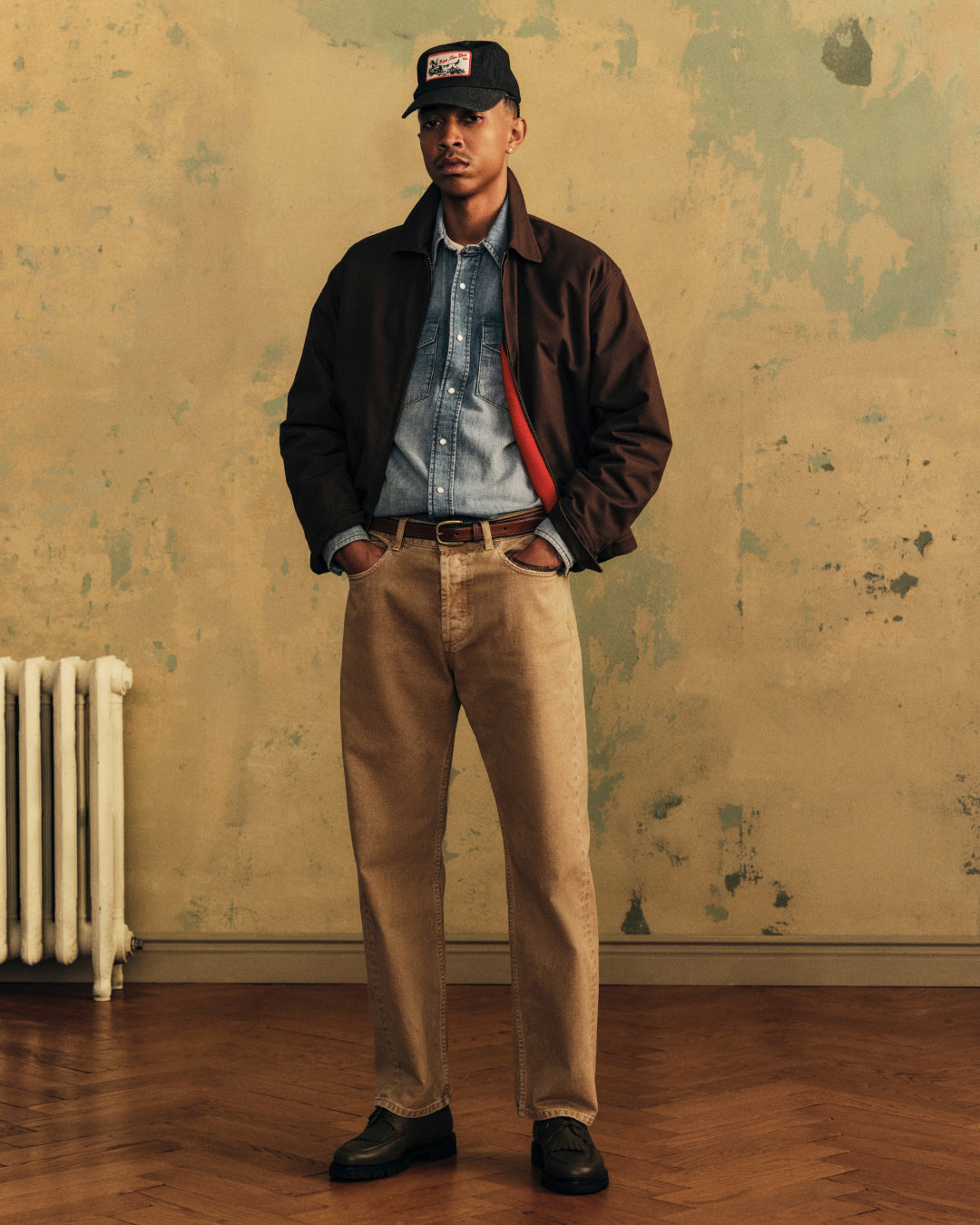 A person wearing a brown Fleece Lined Mechanic Jacket over a denim shirt, tan trousers, and a baseball cap.