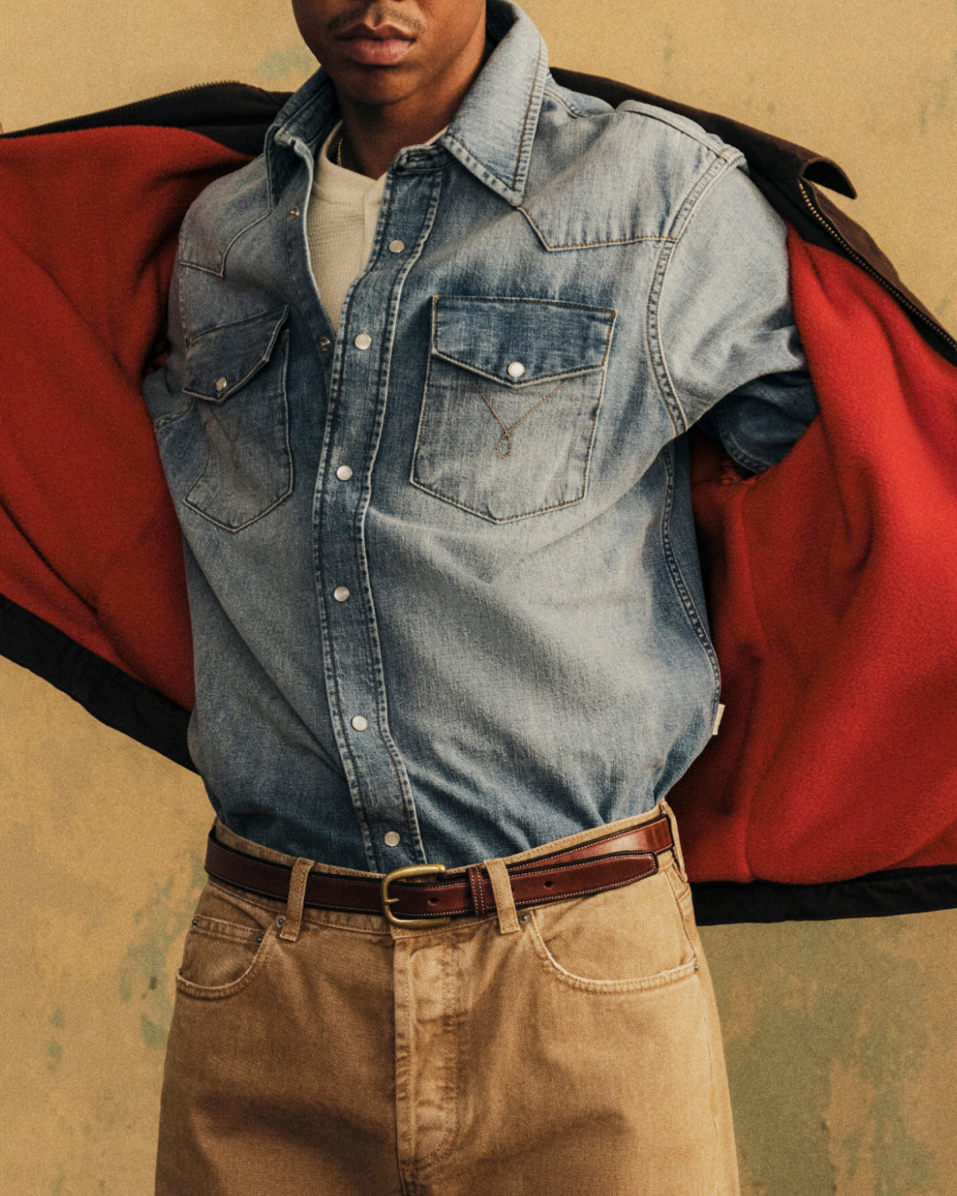 A person in a denim shirt and brown pants displays a Fleece Lined Mechanic Jacket with a bright red fleece interior.
