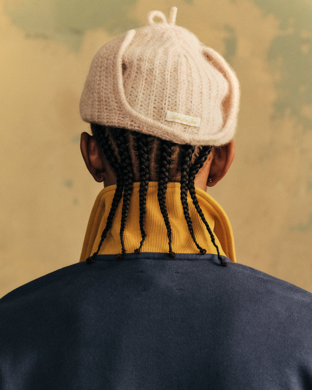 A person wearing a pale pink Alpaca Wool Knit Earflap Hat with a small brand tag on the back.
