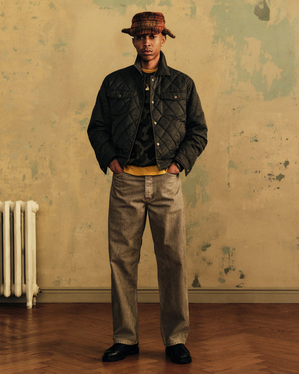 A person wearing a Plaid Wool Hunting Hat, a quilted jacket, a yellow shirt, and loose-fitting jeans.