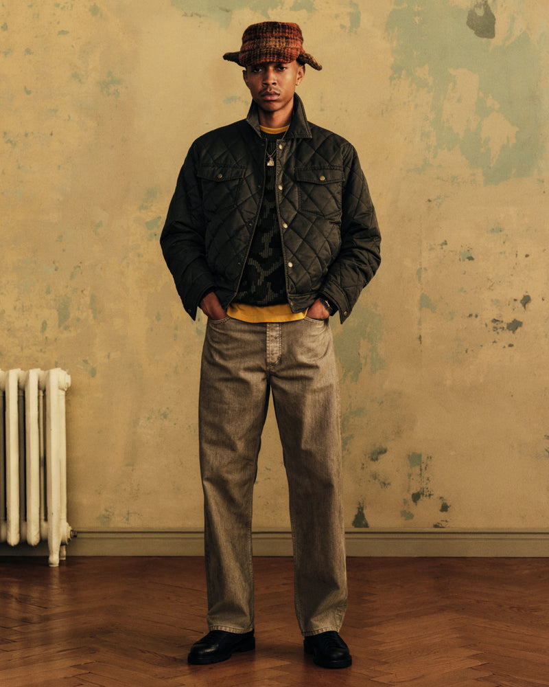 A person wearing a Plaid Wool Hunting Hat, a quilted jacket, a yellow shirt, and loose-fitting jeans.
