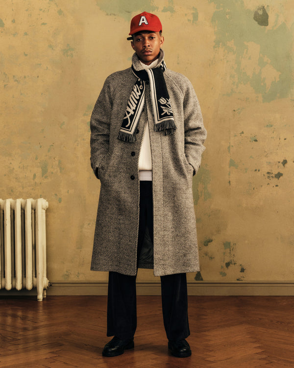 A man wearing a red Wool Varsity Logo Hat, a patterned scarf, and a long herringbone coat.