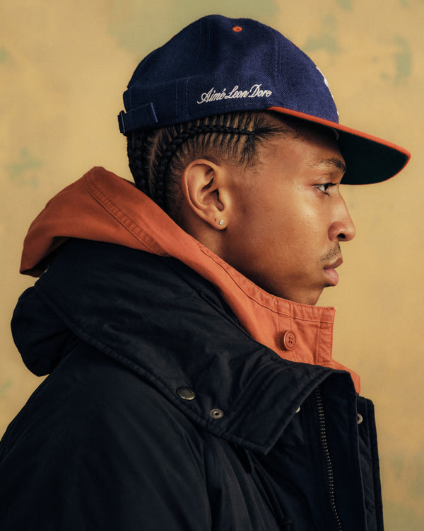 Profile view of a person wearing an ALD / New Era Mets Retro Fit Hat, which is blue with an orange brim and white embroidery.