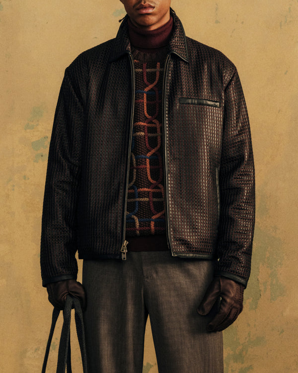 A person wearing a colorful Cable Link Crewneck Sweater layered under a textured zip-up jacket and gloves.