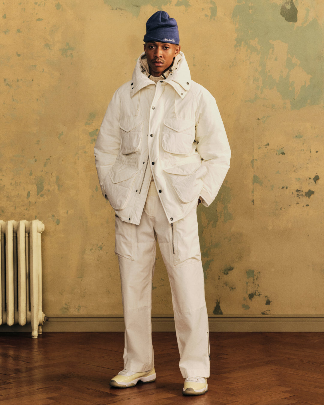 A person wearing a white utility jacket, Garment Washed Aviator Pant, and a blue beanie.