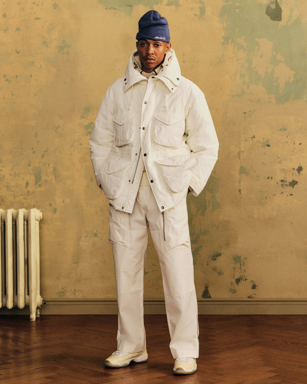 A person wearing a white Down-Filled Surplus Parka and matching trousers with a blue beanie.