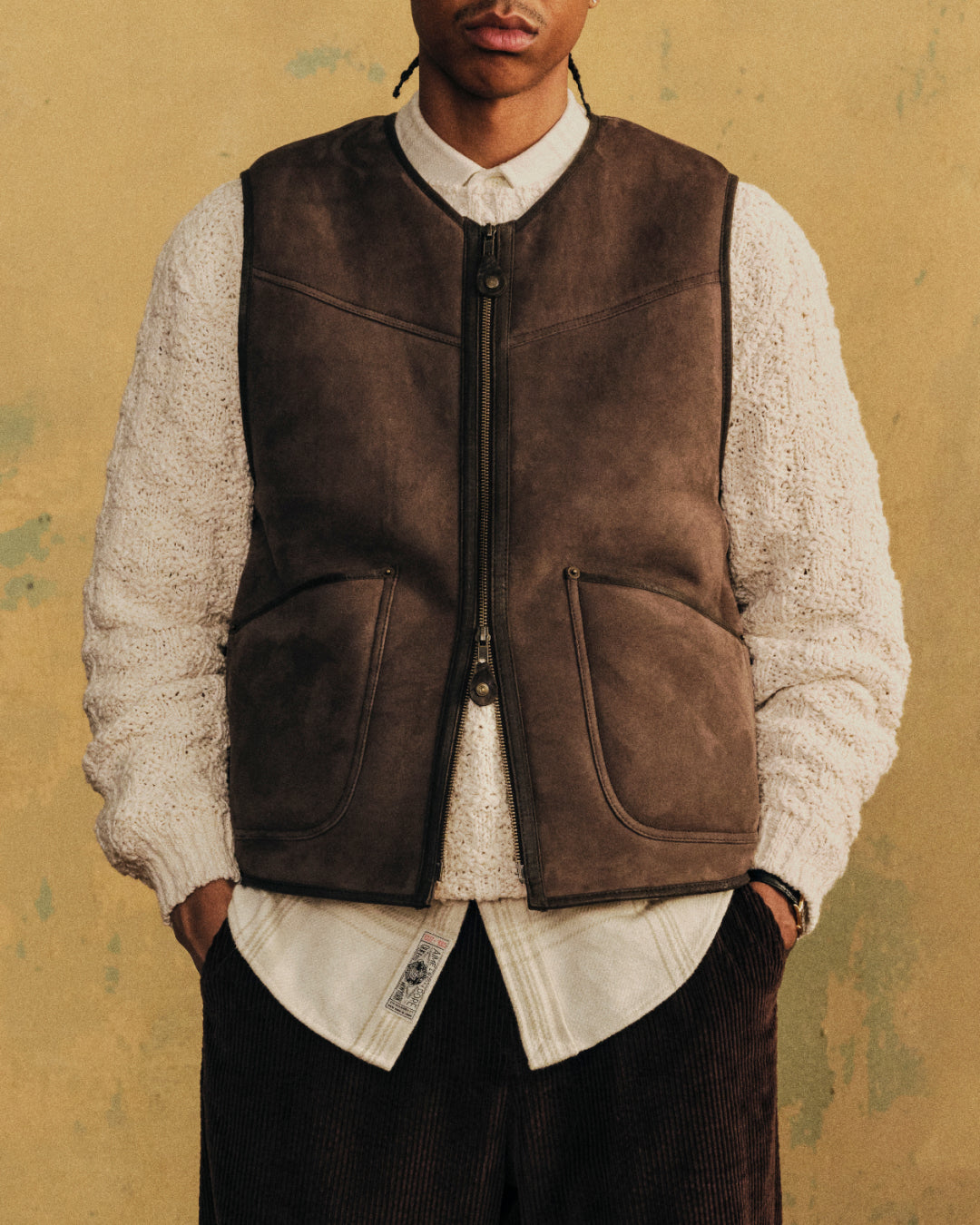 A man wears a brown Shearling Biker Vest over a white sweater and collared shirt.