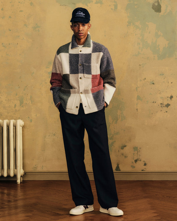 A man in a Corduroy Unisphere Hat, patchwork button-down jacket, dark trousers, and white sneakers.