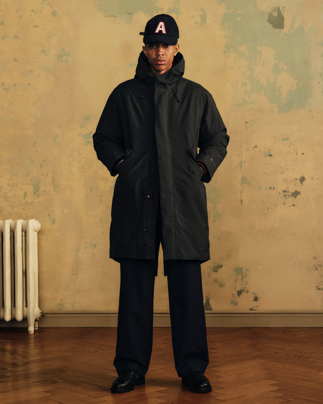 Person wearing a black Wool Varsity Logo Hat with a red letter A, a black hooded coat, and dark trousers.