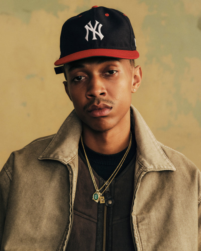 A man wearing an ALD / New Era Yankees Retro Fit Hat, a navy baseball cap with a red brim and a white NY logo.