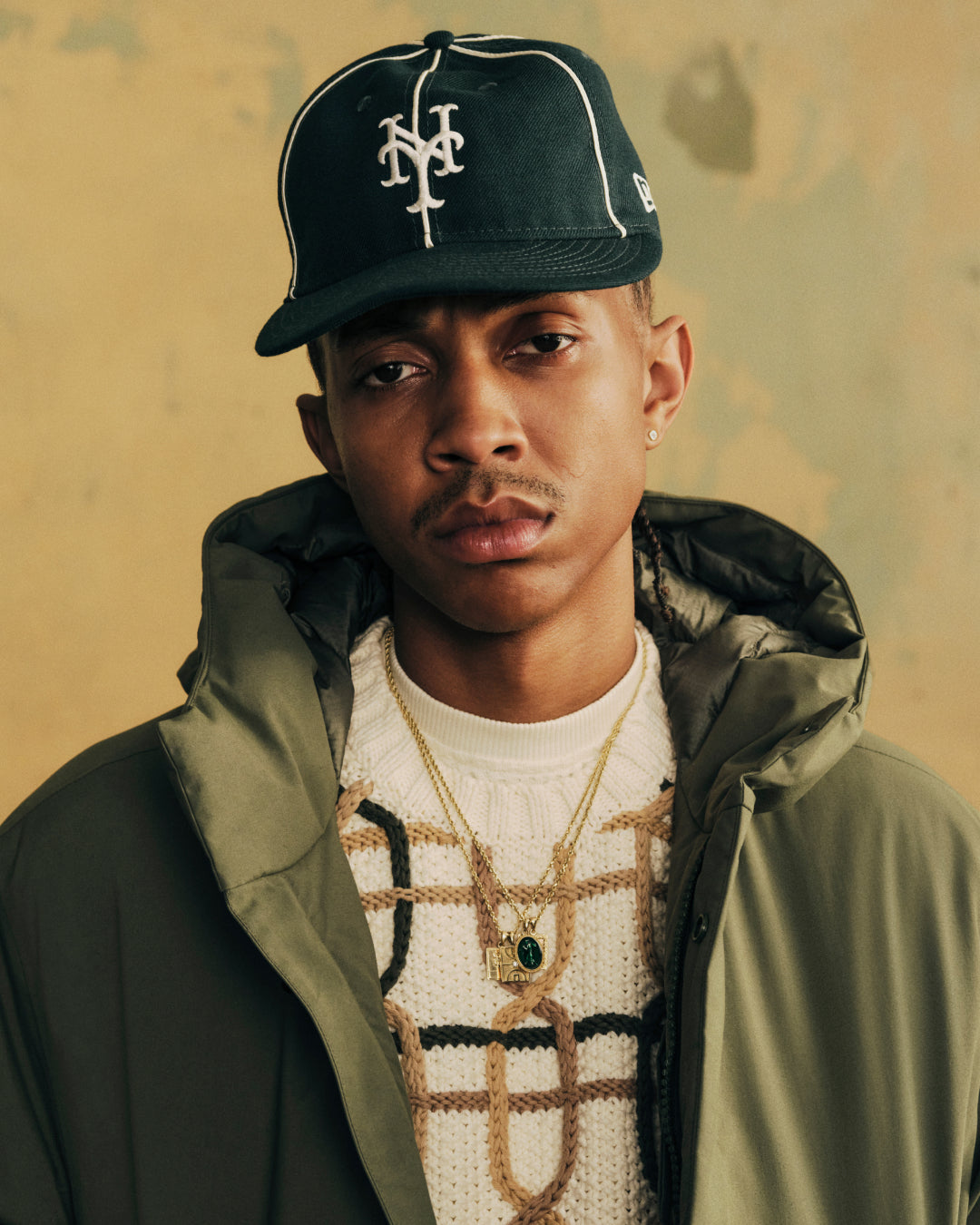 A person wearing an ALD / New Era Mets Wool Hat and an olive green hooded jacket.