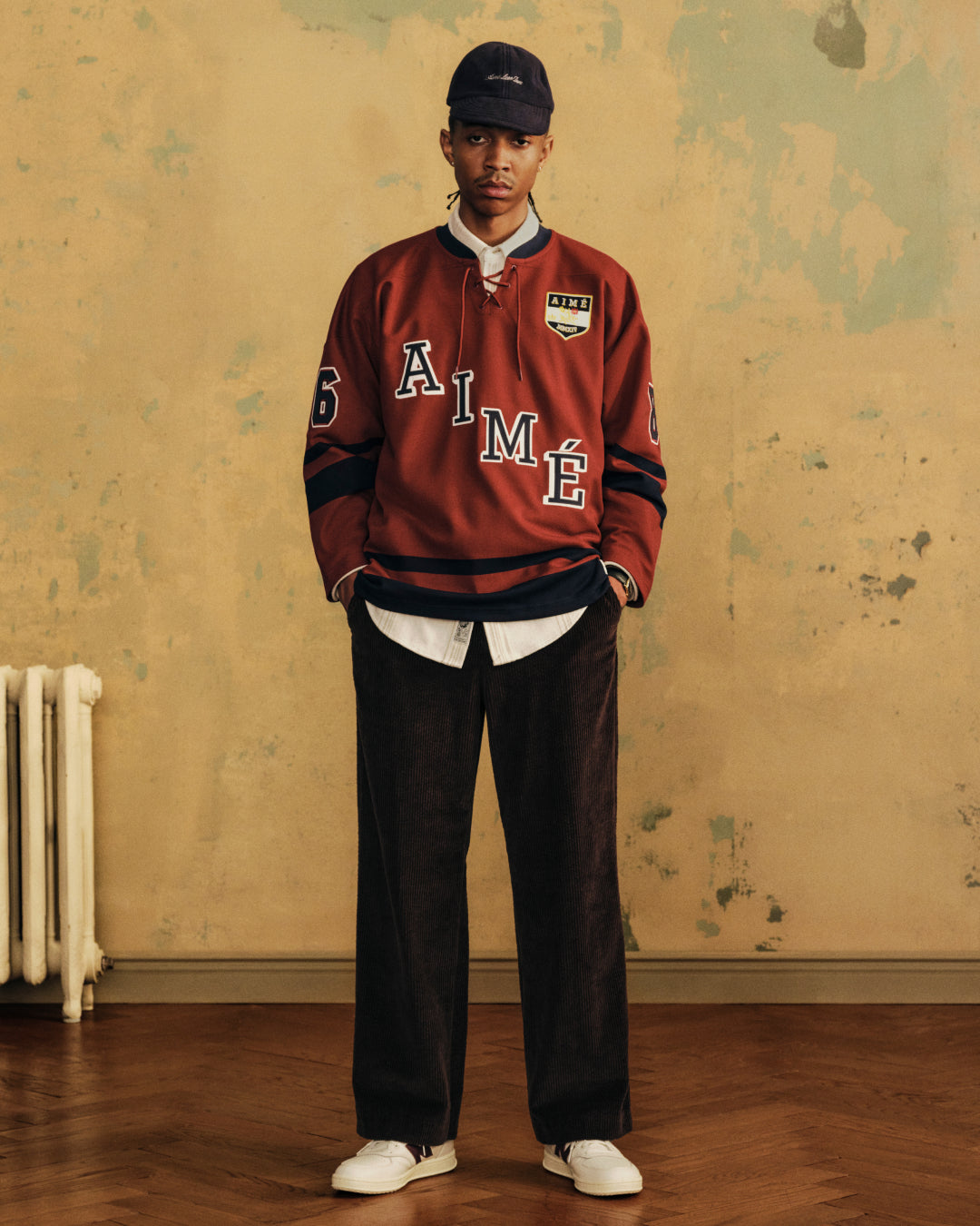 A person wearing a dark Script Fleece Hat, a red long-sleeve jersey, a white collared shirt, and dark trousers.