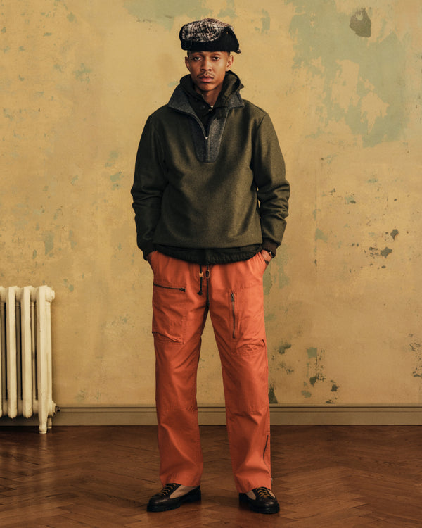 A person wearing a dark green quarter-zip pullover and bright orange Garment Washed Aviator cargo pants with zippers.