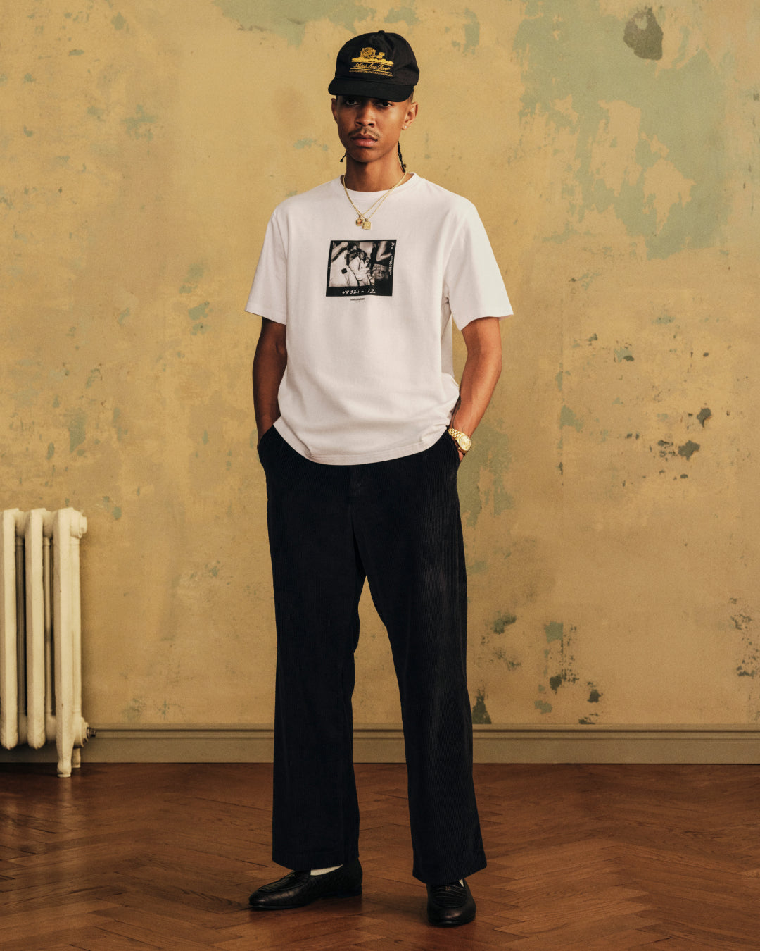 A person wearing The Esco Tee, dark trousers, and a baseball cap.