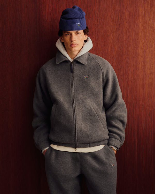 Someone wears the Crest Fleece Casual Jacket in gray and poses against a wooden wall, styled with matching pants.