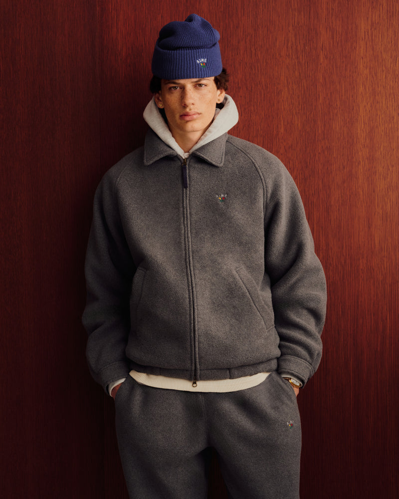 Someone wears the Crest Fleece Casual Jacket in gray and poses against a wooden wall, styled with matching pants.