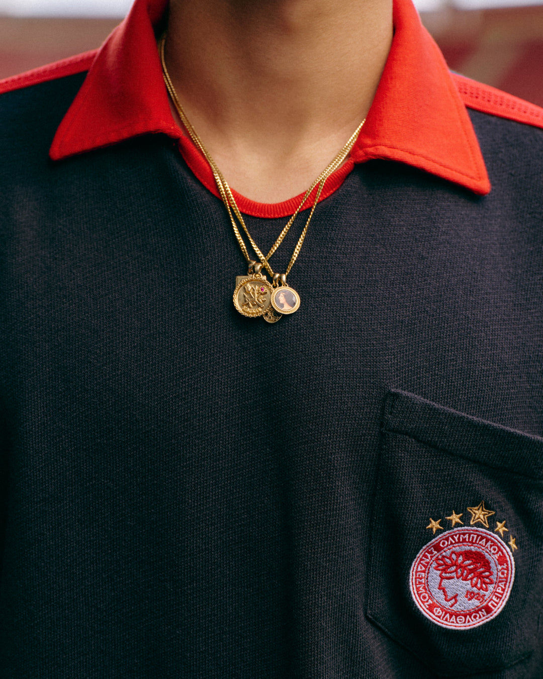 Close-up of the ALD / Olympiacos F.C. Heritage Ringer Polo, a black shirt with a red collar and circular chest crest.