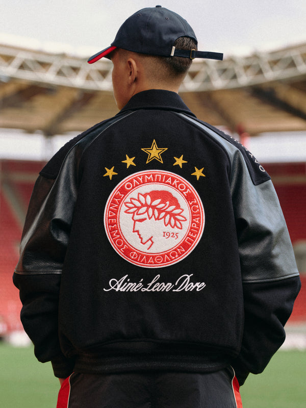 Person wearing an ALD / Olympiacos F.C. Team Leather Jacket with a red and white club emblem on the back.