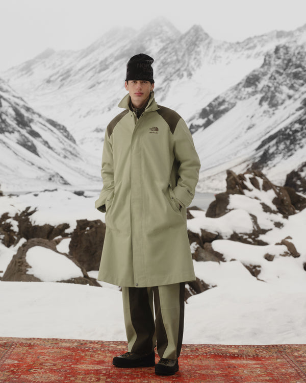 A person in an ALD/The North Face GORE-TEX Trench Coat stands on a rug in a snowy mountain landscape.