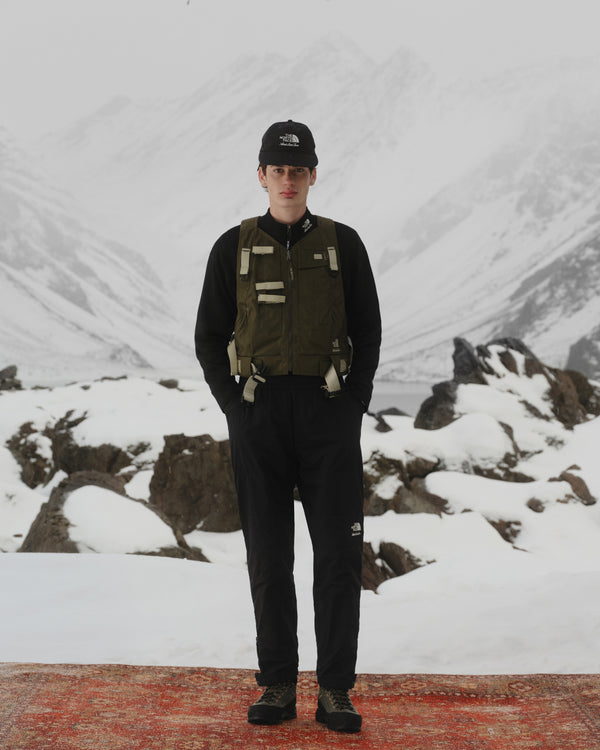 A person in outdoor gear wears the ALD / The North Face Nylon Logo Hat with snowy mountains and rocks behind.