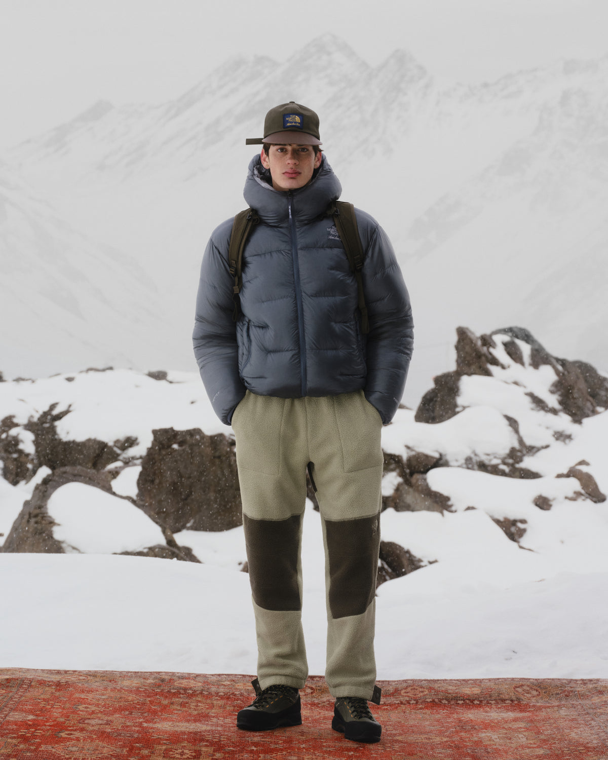 A person wearing ALD / The North Face Denali Fleece Pant stands outdoors with snowy mountains and rocks behind them.