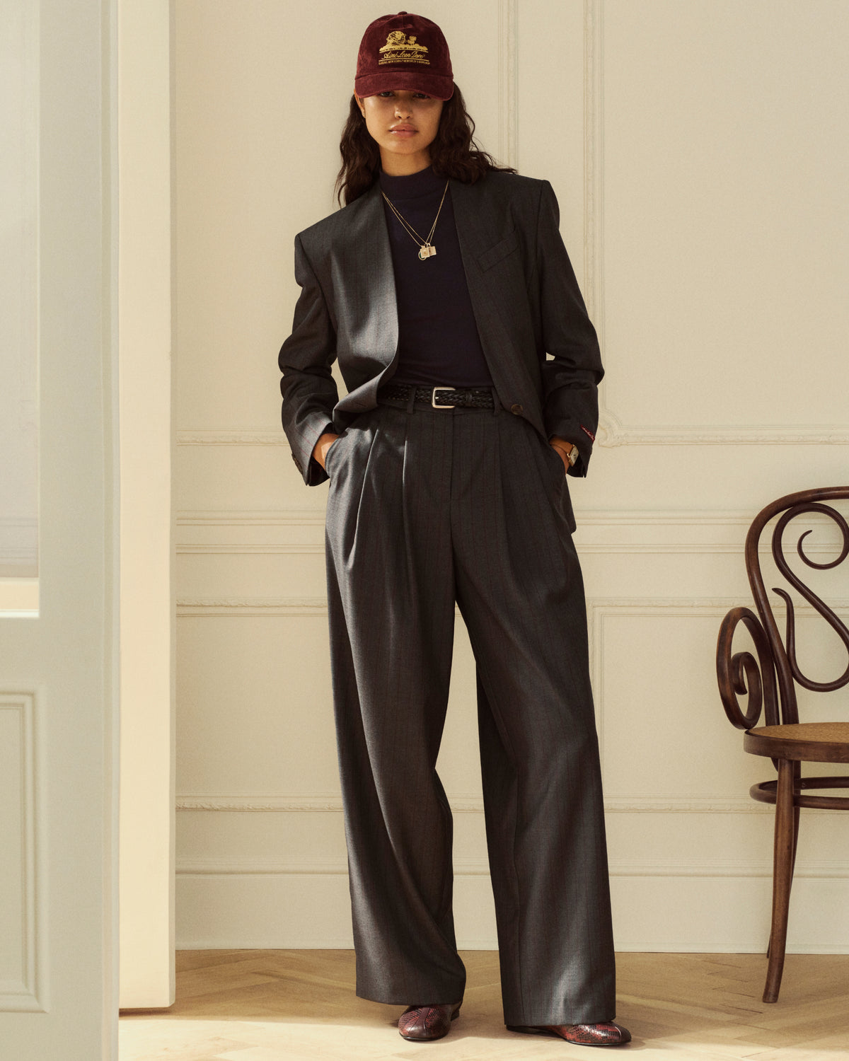 A person wears a charcoal grey Collarless Striped Blazer and matching trousers over a dark turtleneck and baseball cap.