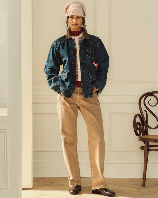 Person wearing a Denim Chore Coat, patterned sweater, and tan trousers with a beanie.