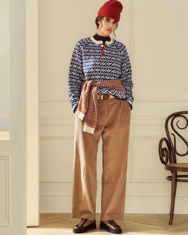 A person in a red beanie and patterned sweater wearing Double Pleated Corduroy Trousers with hands in their pockets.