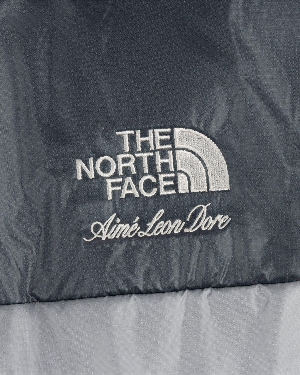 Close-up of ALD / The North Face Reversible Pertex® Nuptse Jacket logo embroidered on gray fabric.