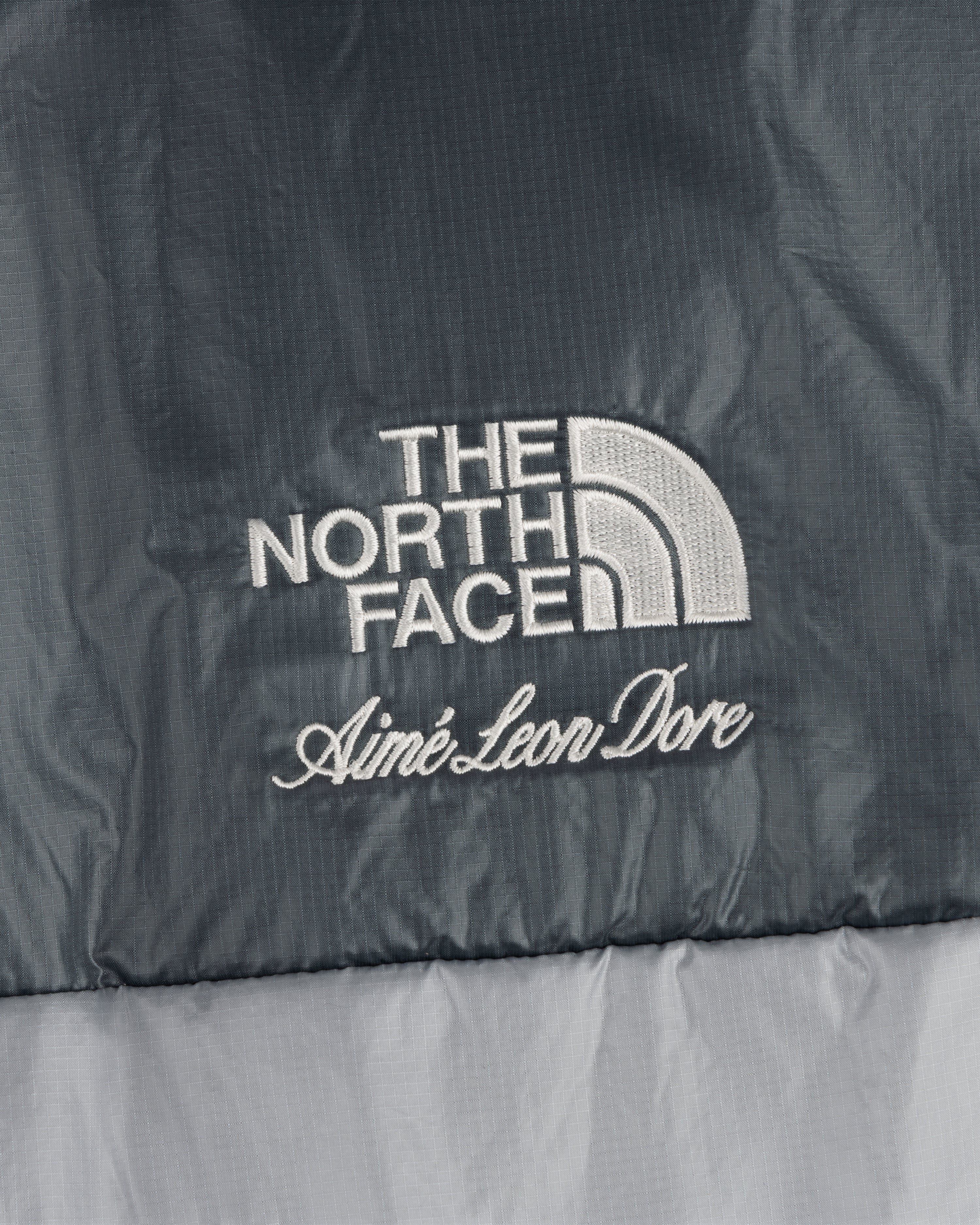 Close-up of ALD / The North Face Reversible Pertex® Nuptse Jacket logo embroidered on gray fabric.