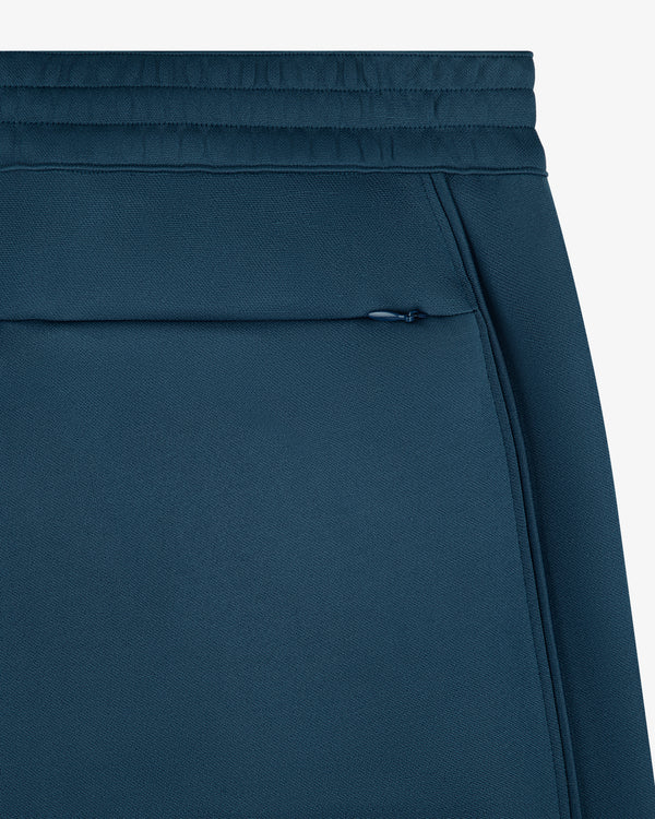 Close-up of ALD / New Balance RC56 Track Pant showing waistband, zip side pocket, and textured blue fabric.