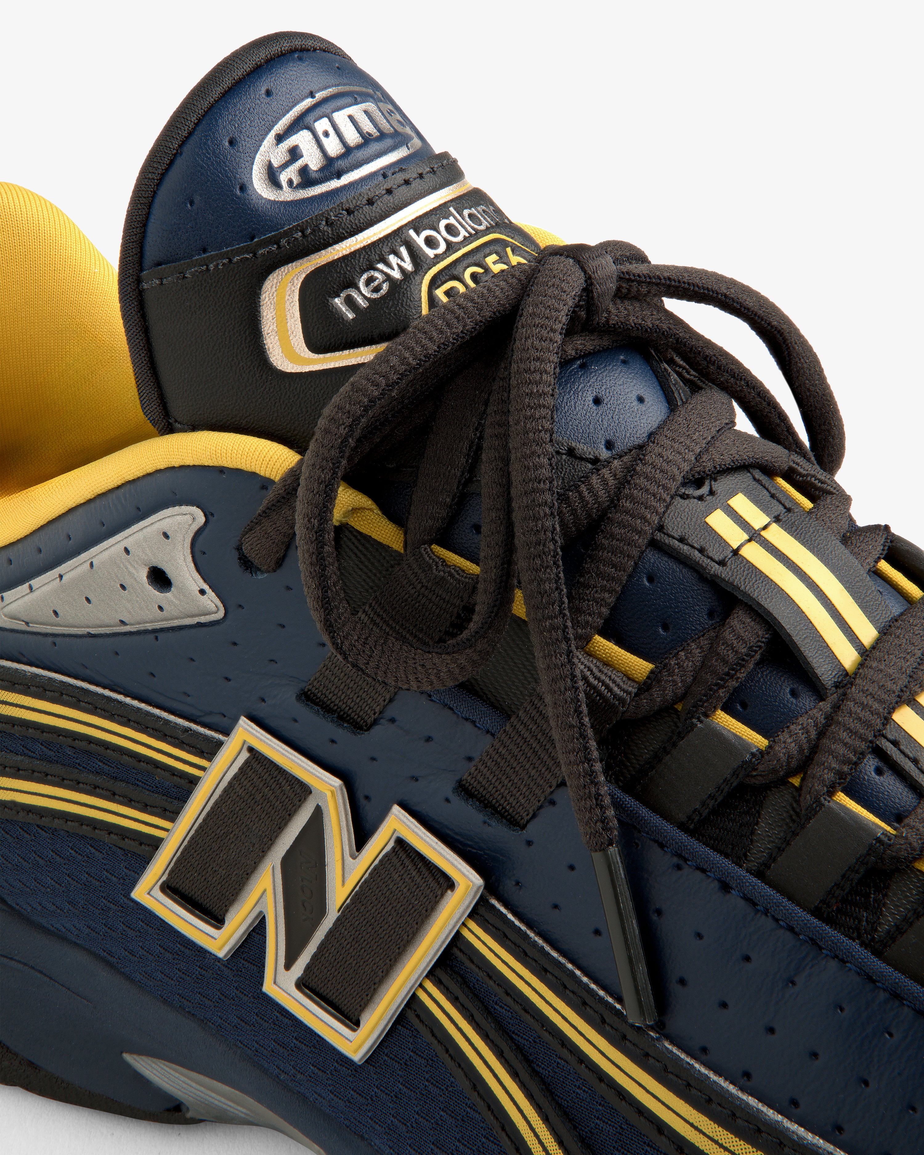 Close-up of a navy and yellow ALD / New Balance RC56 sneaker with black laces and prominent logo.