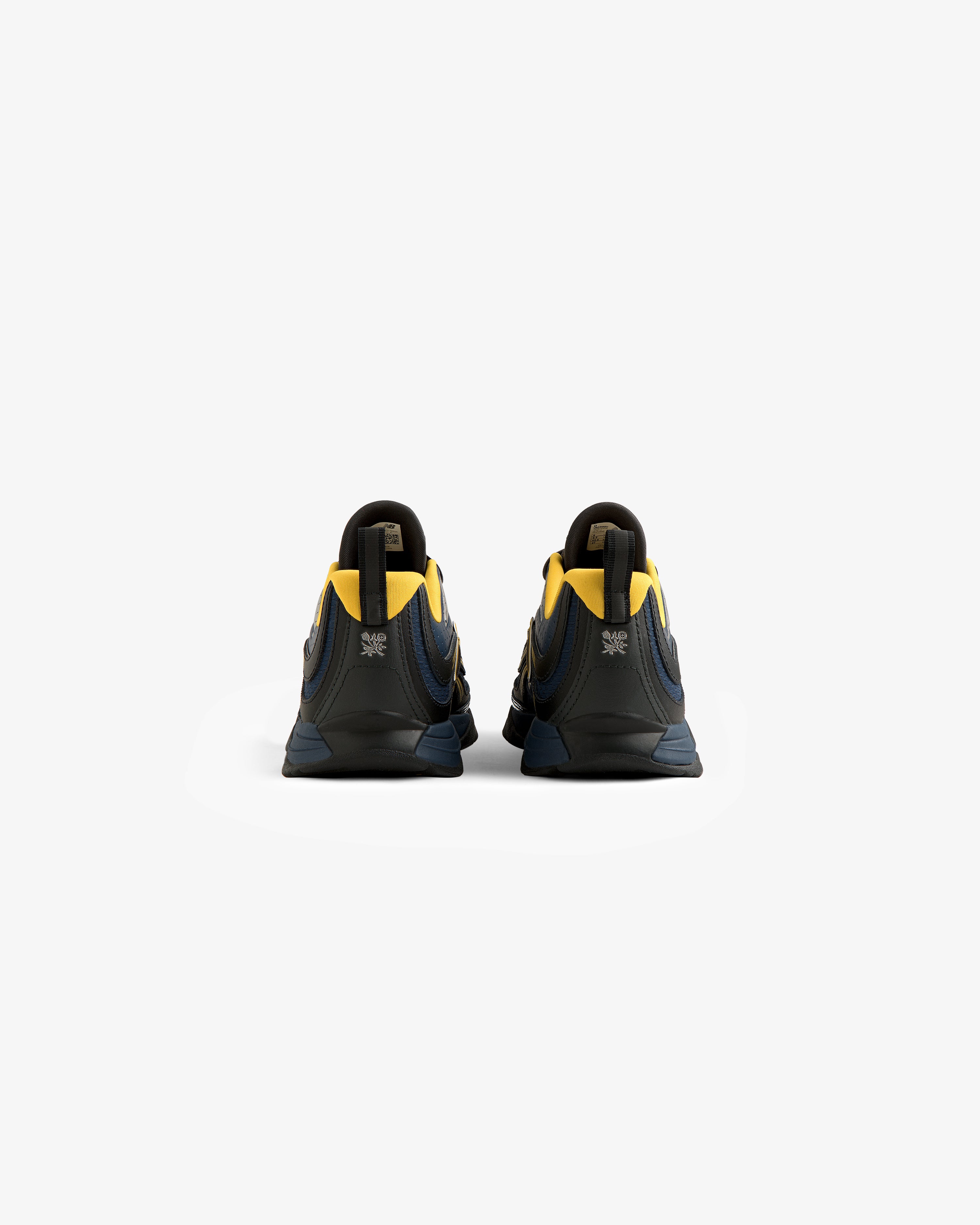 The ALD / New Balance RC56 sneakers in dark blue and yellow are shown from the back on a plain white background.
