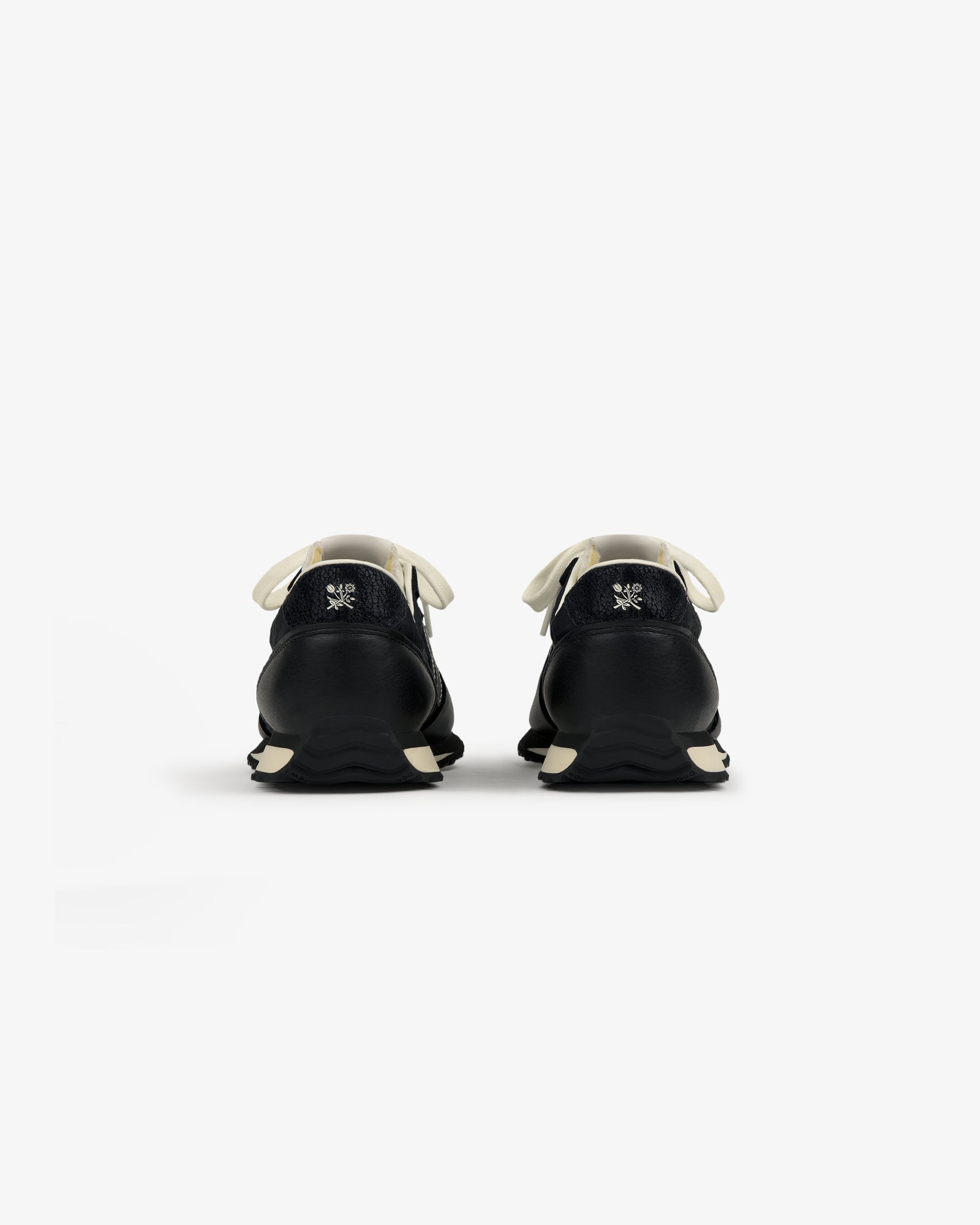 Rear view of ALD / New Balance 471 sneakers in black with white laces, soles, and a small logo embroidered on each heel.
