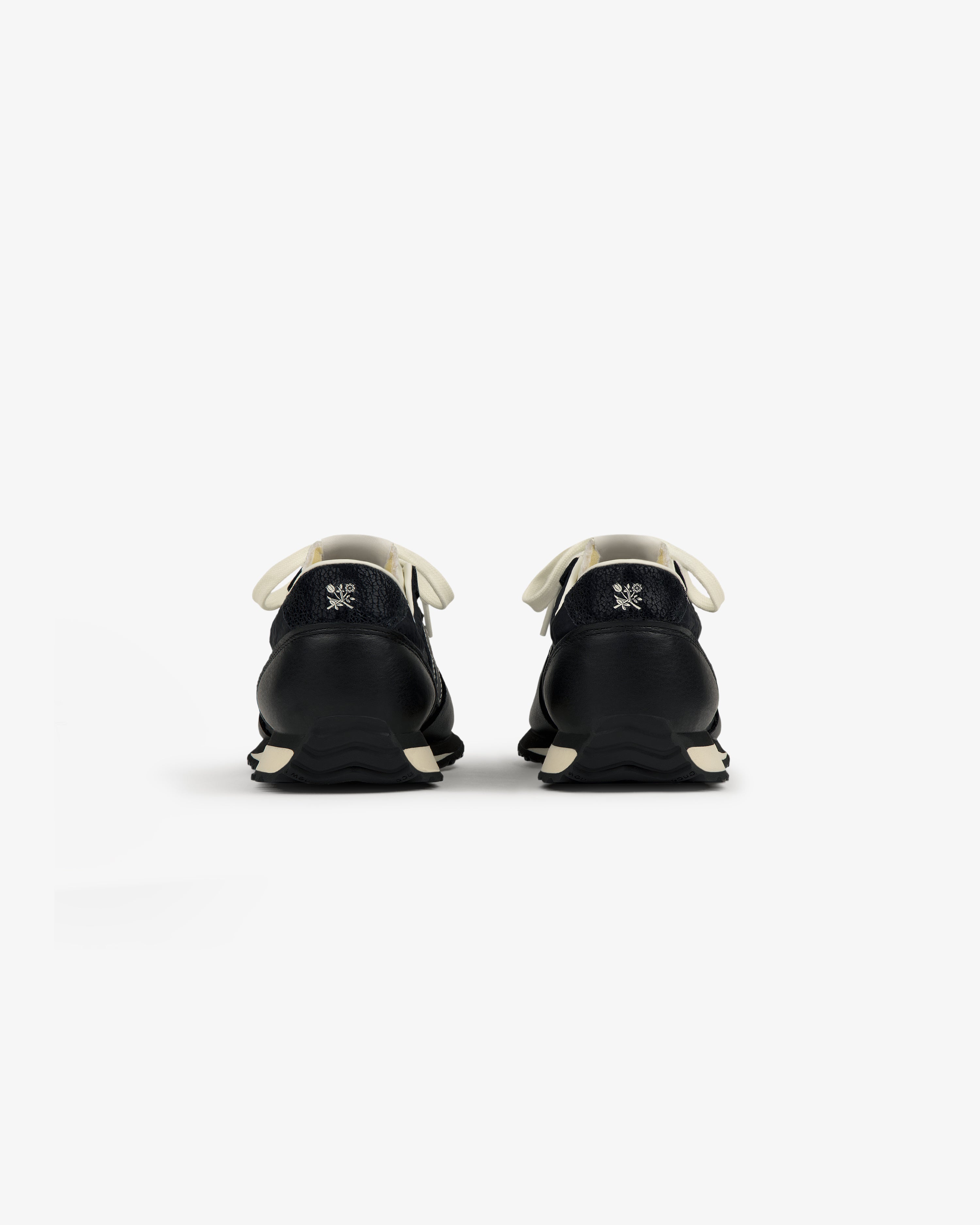 Rear view of ALD / New Balance 471 sneakers in black with white laces, soles, and a small logo embroidered on each heel.