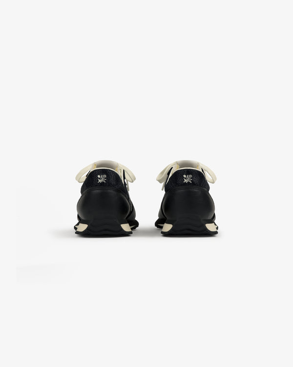 Rear view of ALD / New Balance 471 sneakers in black with white laces, soles, and a small logo embroidered on each heel.
