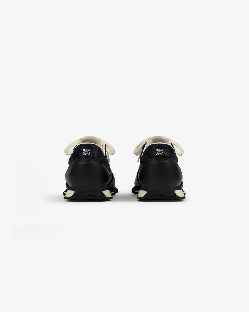 Rear view of ALD / New Balance 471 sneakers in black with white laces, soles, and a small logo embroidered on each heel.