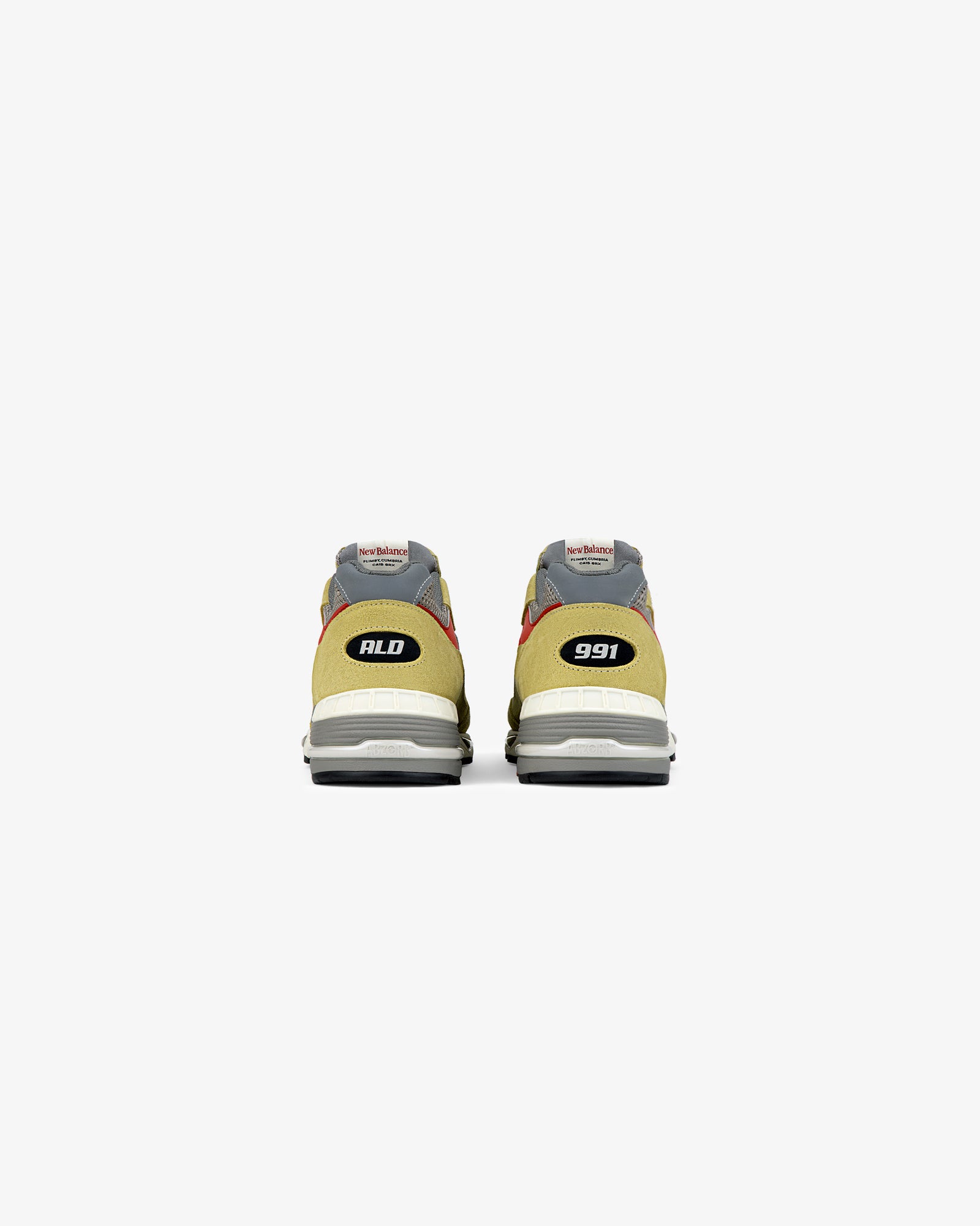 A pair of yellow and gray ALD / New Balance Made in UK 991 sneakers seen from the back, with ALD and 991 on the heels.