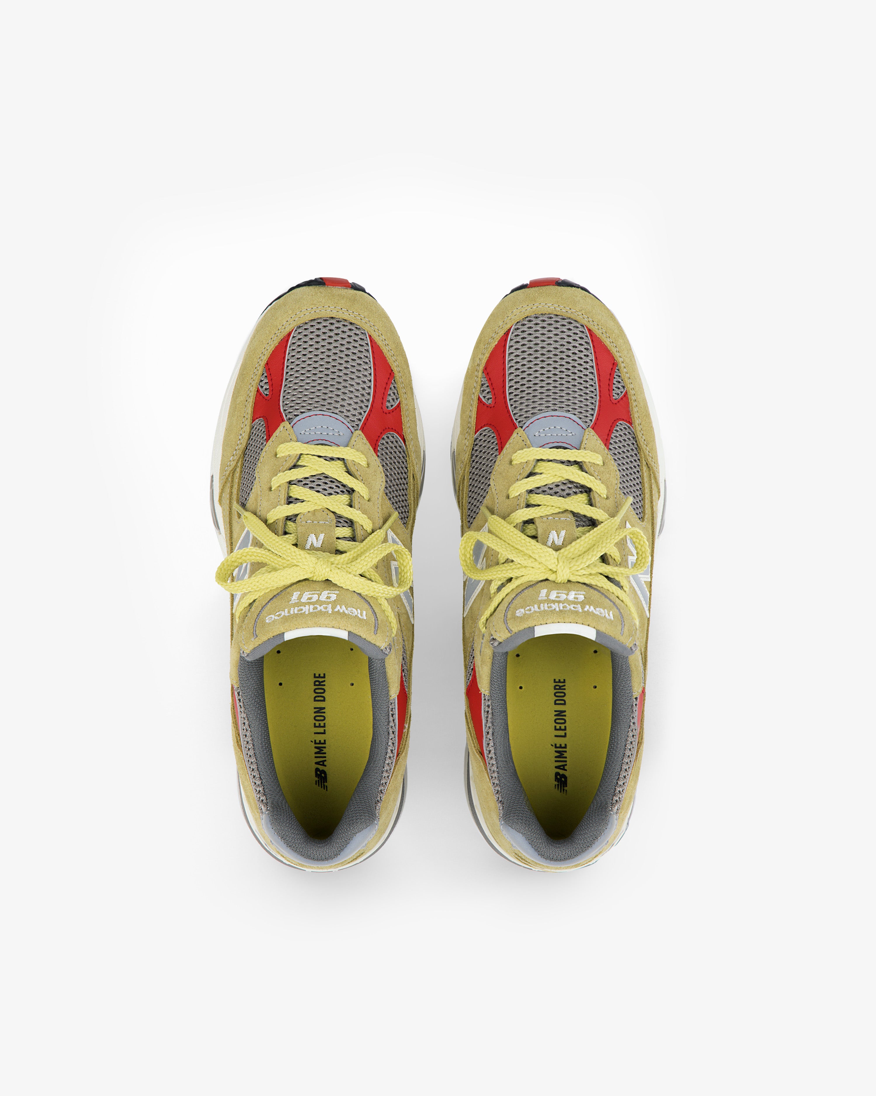 ALD / New Balance Made in UK 991 sneakers with yellow laces, gray mesh, red and yellow accents, top view on white.