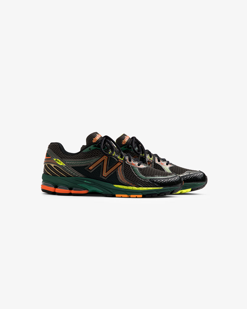 A pair of ALD / New Balance 860v2 sneakers in black and green with orange and yellow accents on a white background.